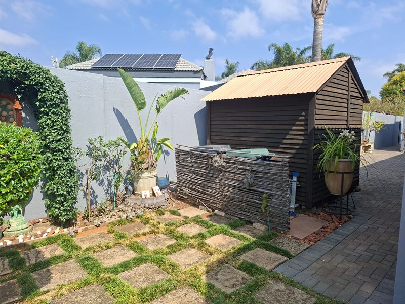 A well-maintained rear garden area featuring a timber storage shed, paved pathways, and a secure boundary wall with integrated solar panels on the roof.