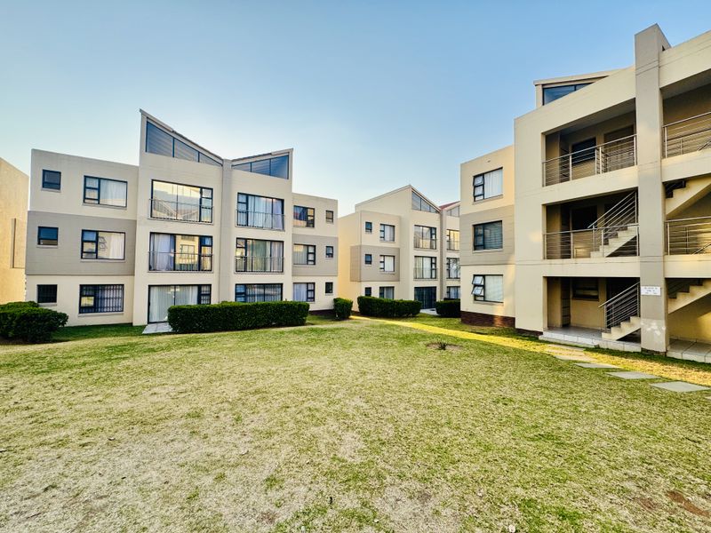 A view of the rear exterior of a modern apartment complex featuring multi-story buildings, balconies, external staircases, and a well-maintained communal lawn area.