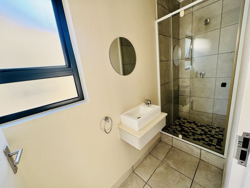 A clean, modern bathroom featuring a glass-enclosed shower, wall-mounted basin, and neutral tiled finishes.