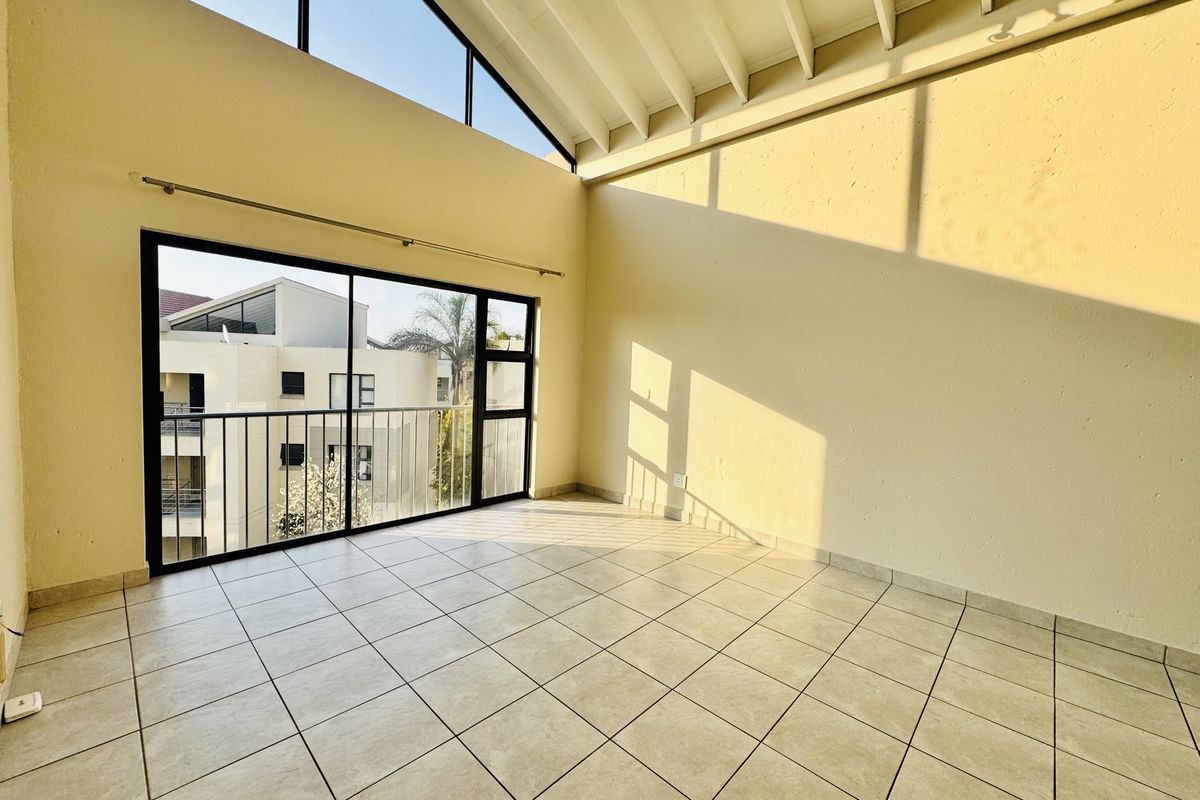 Spacious living area featuring high vaulted ceilings with exposed rafters, tiled flooring, and a large sliding door leading to a private balcony.