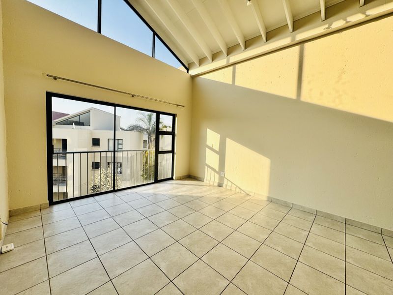 Spacious living area featuring high vaulted ceilings with exposed rafters, tiled flooring, and a large sliding door leading to a private balcony.