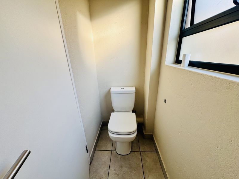 A compact, functional bathroom featuring a standard toilet, tiled flooring, and a window for natural light.
