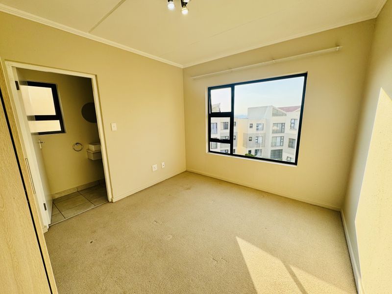An empty bedroom featuring carpeted flooring, a large aluminium-framed window, and direct access to an en-suite bathroom.