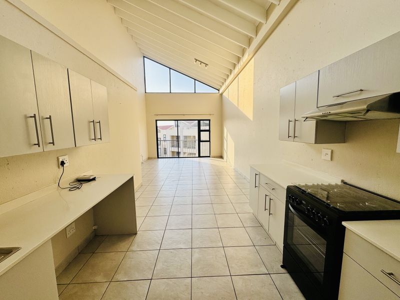 Spacious open-plan kitchen and living area featuring high vaulted ceilings, tiled floors, and large windows providing ample natural light.