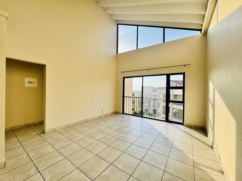 Spacious living area featuring high vaulted ceilings with exposed rafters, tiled flooring, and large sliding doors leading to a balcony with natural light.
