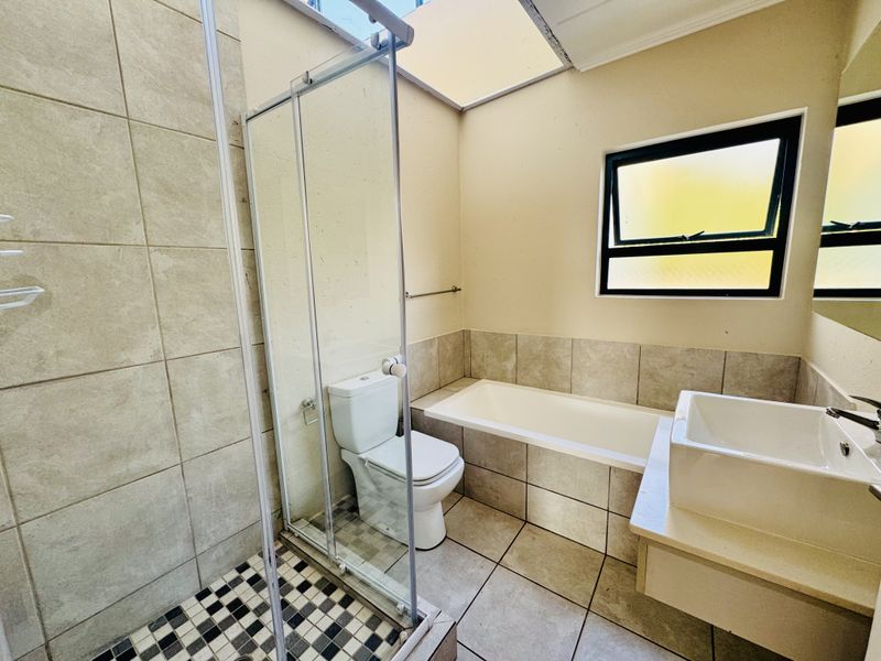 A functional bathroom featuring a separate shower enclosure, bathtub, vanity basin, and a skylight providing natural light.