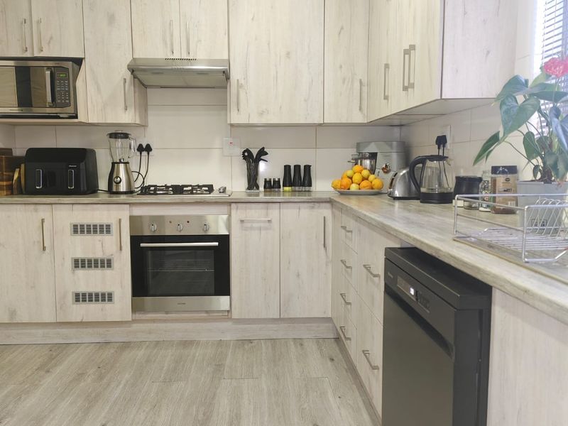 Modern kitchen featuring light wood-grain cabinetry, laminate countertops, built-in oven, gas hob, and integrated dishwasher with durable laminate flooring.