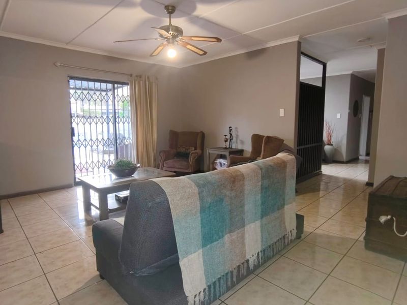 A living room featuring tiled flooring, a ceiling fan, and a sliding glass door with a security gate leading to the exterior.