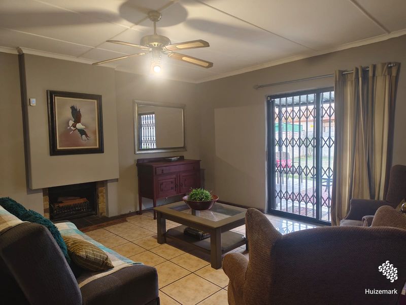 A comfortable living room featuring a built-in fireplace, tiled flooring, and a sliding glass door with a security gate leading to the outdoor area.
