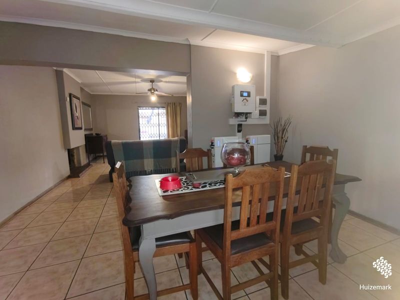 Open-plan dining and living area featuring tiled flooring, a built-in fireplace, and a wall-mounted inverter and battery backup system.
