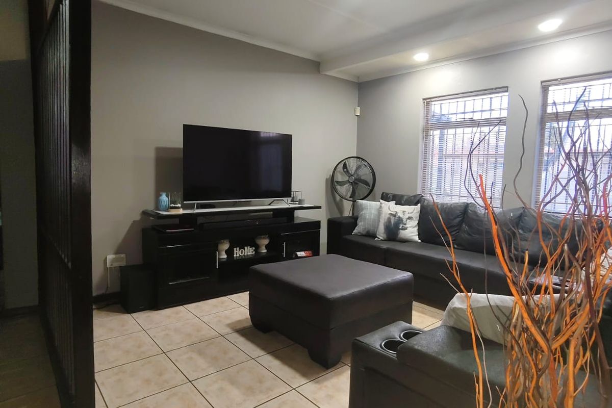 A comfortable living room featuring tiled flooring, recessed ceiling lighting, and windows fitted with security bars.