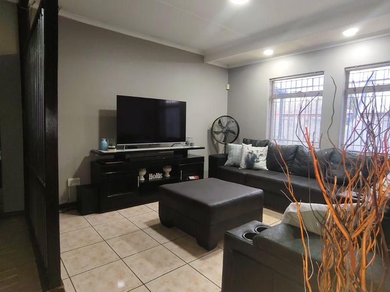 A comfortable living room featuring tiled flooring, recessed ceiling lighting, and windows fitted with security bars.