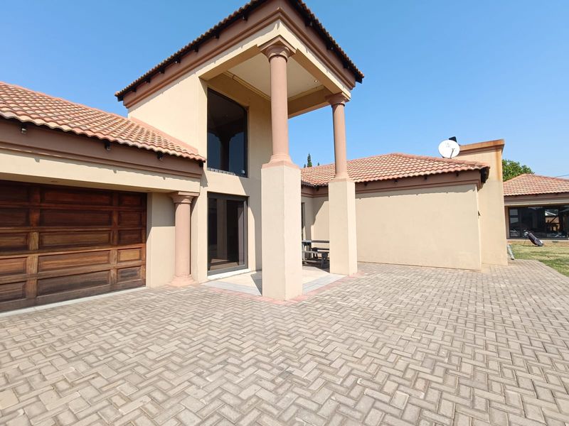 Front elevation of a modern house featuring a paved driveway, wooden garage door, and a covered entrance with architectural columns.