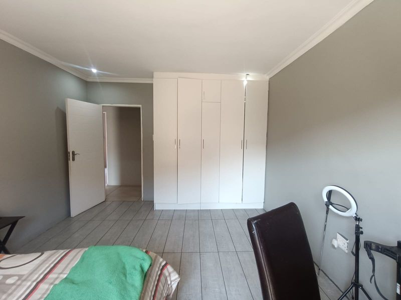 A bedroom featuring neutral grey walls, tiled flooring, and white built-in cupboards providing ample storage space.