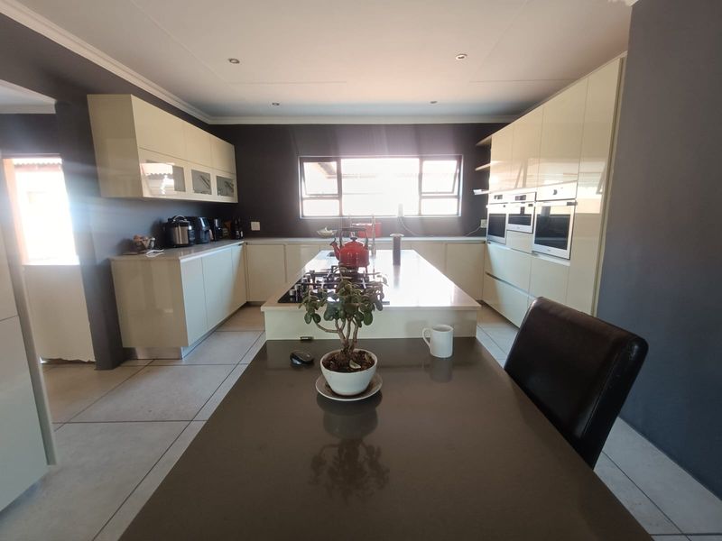 Modern kitchen featuring high-gloss cabinetry, a central island with a gas hob, stone countertops, and integrated built-in ovens.
