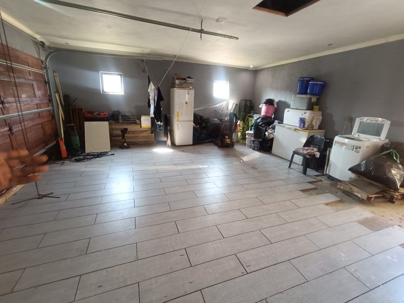 Spacious garage featuring modern grey tiled flooring, a sectional garage door, and ceiling access, currently used for storage and utility purposes.