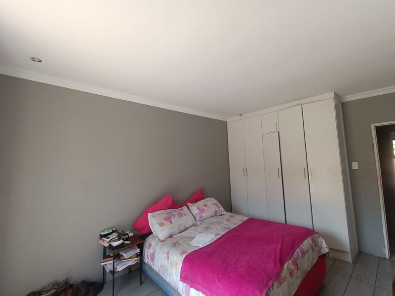 A bedroom featuring built-in cupboards, tiled flooring, and recessed downlighting, providing a functional and neutral space.