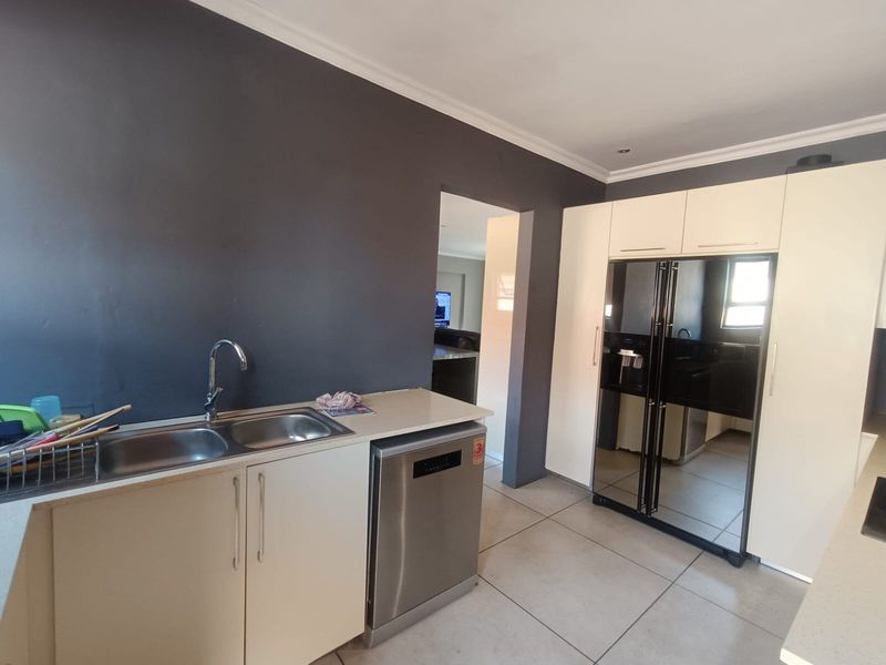 Modern kitchen featuring sleek white cabinetry, stone countertops, double bowl sink, and tiled flooring, with a clean, contemporary aesthetic.