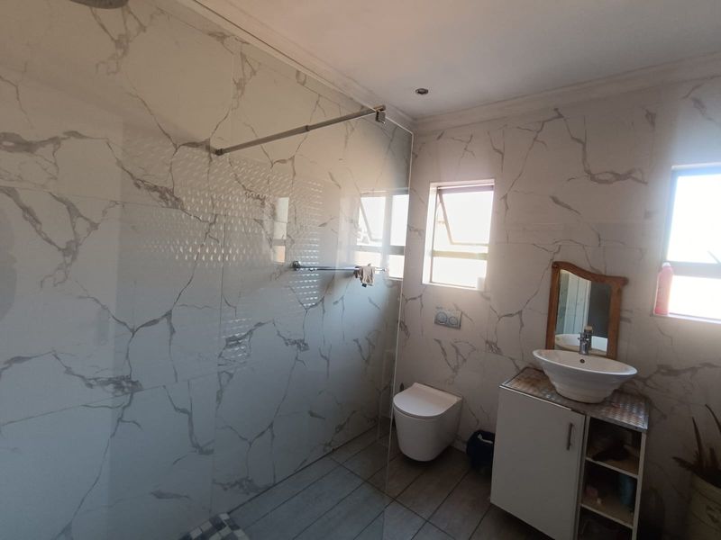 Modern bathroom featuring marble-effect wall tiling, a spacious walk-in shower with glass screen, wall-mounted toilet, and a contemporary vessel sink vanity unit.