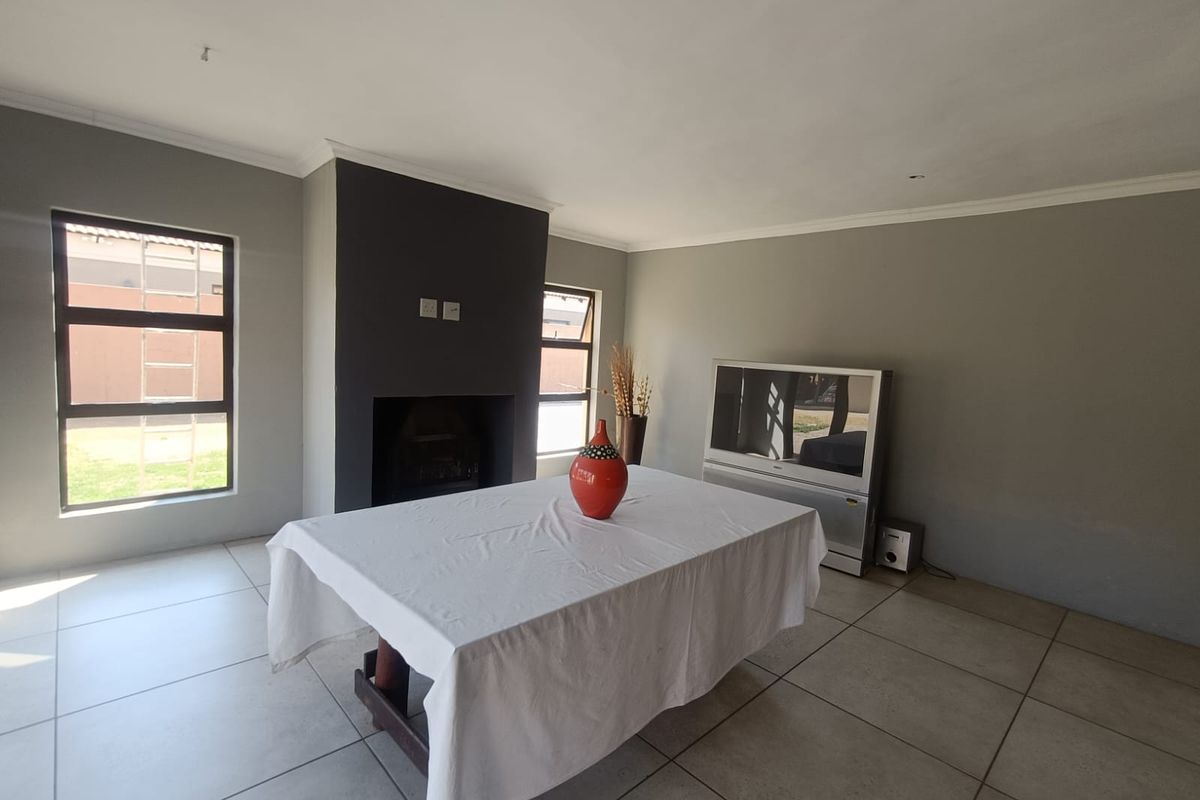 A living room featuring tiled flooring, a central fireplace with a dark feature wall, and large aluminium-framed windows providing natural light.