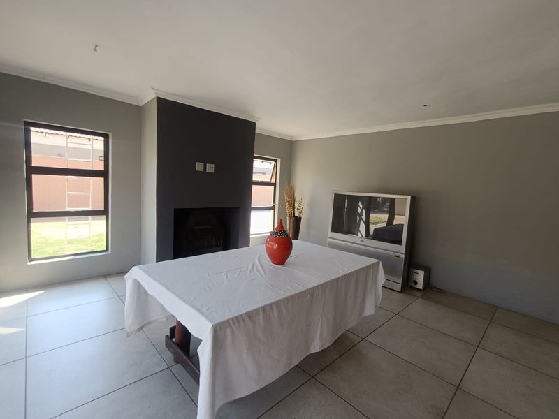 A living room featuring tiled flooring, a central fireplace with a dark feature wall, and large aluminium-framed windows providing natural light.