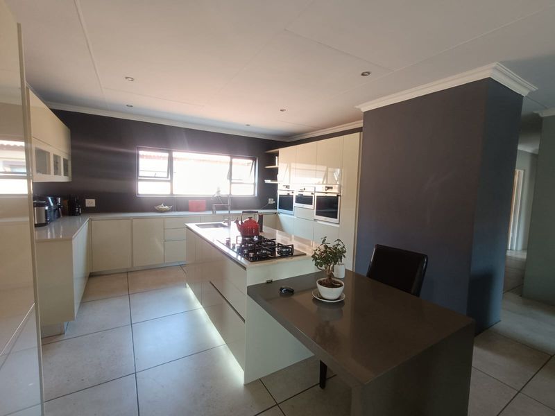 Modern kitchen featuring a central island with a gas hob, integrated ovens, stone countertops, and sleek cabinetry with recessed lighting.