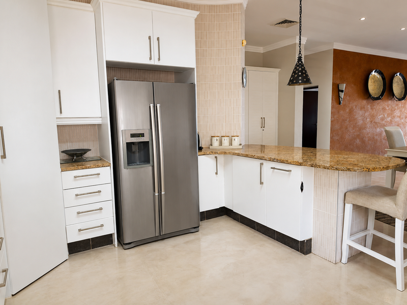 Modern kitchen featuring granite countertops, white cabinetry, and a stainless steel side-by-side refrigerator with integrated lighting.