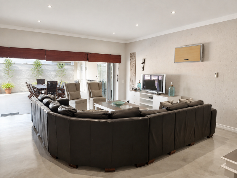 Spacious living room featuring polished concrete floors, recessed lighting, and large stacking glass doors that open onto an outdoor patio area.