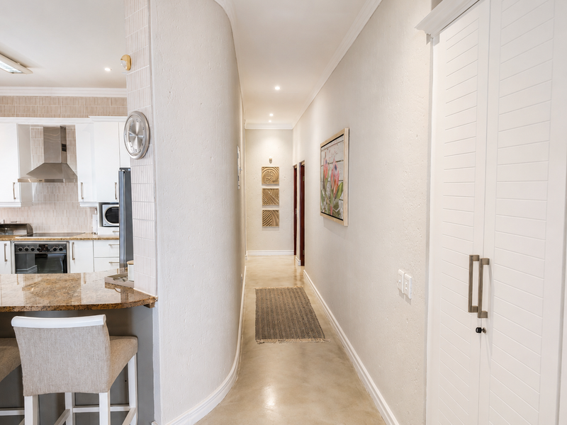 A bright hallway featuring polished concrete floors and a unique curved wall, leading towards a modern kitchen with granite countertops and built-in appliances.