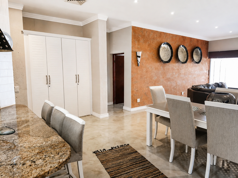Spacious open-plan living and dining area featuring polished concrete floors, granite breakfast bar, built-in cabinetry, and elegant textured feature wall.