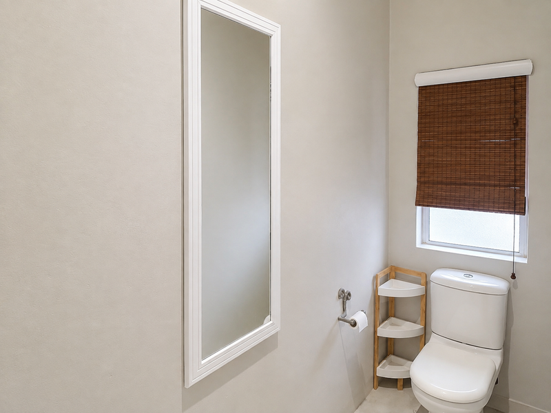 A clean and well-maintained bathroom featuring a modern toilet, a wall-mounted mirror, and a window with a bamboo roller blind.