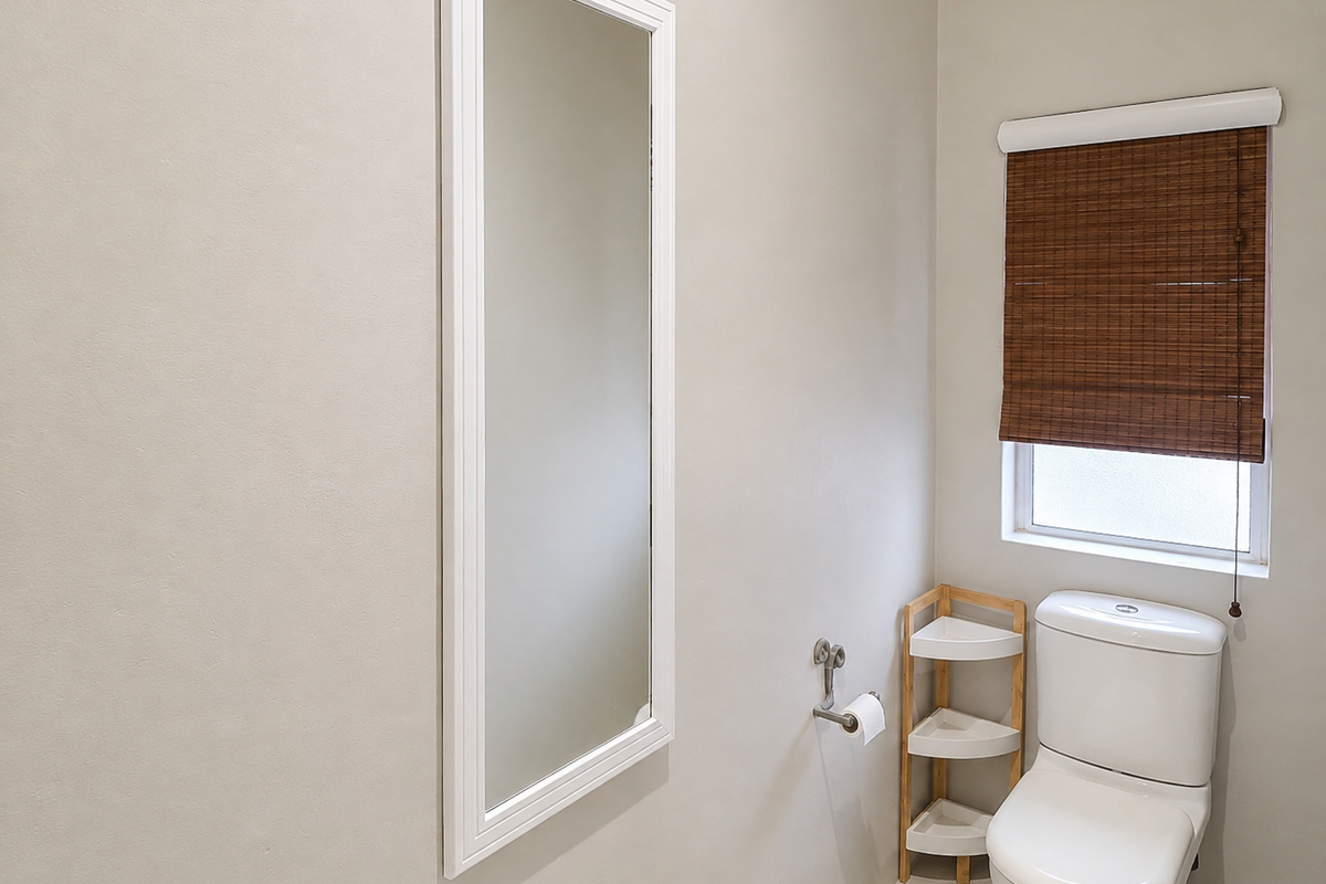 A clean and well-maintained bathroom featuring a modern toilet, a wall-mounted mirror, and a window with a bamboo roller blind.