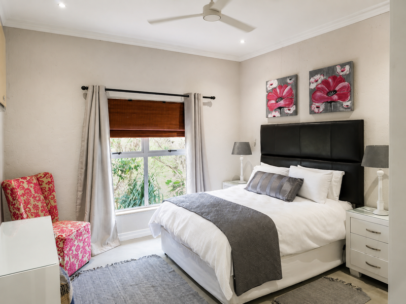 A well-maintained bedroom featuring neutral walls, recessed downlighting, a ceiling fan, and large windows providing natural light and garden views.