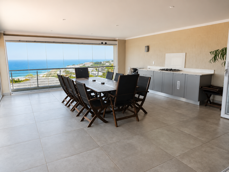 Spacious covered balcony featuring a built-in kitchenette with gas hob, stone countertops, and expansive glass sliding doors offering panoramic ocean views.