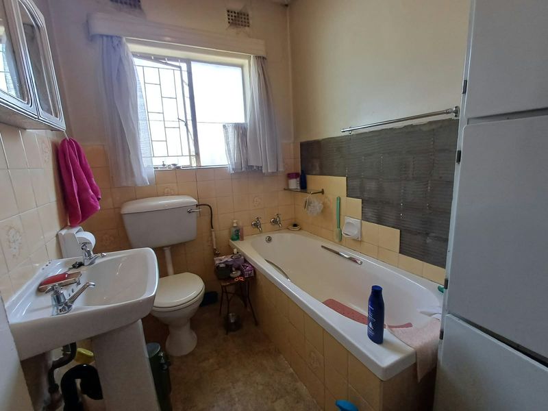 A dated bathroom featuring a pedestal basin, toilet, and bathtub with partially missing wall tiles, requiring renovation to update finishes and fixtures.