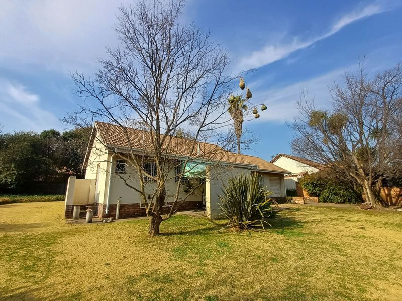 Rear view of the house featuring a tiled roof, brick accents, and a small concrete patio area set within a large garden.
