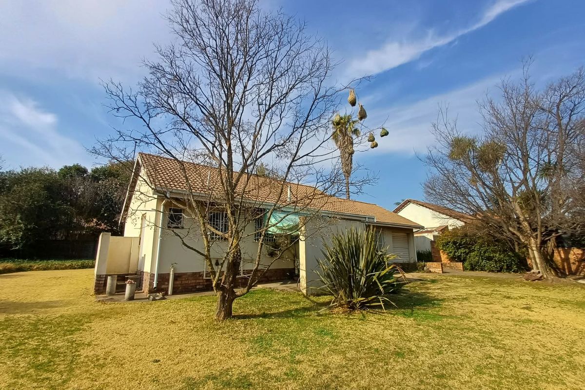Rear view of the house featuring a tiled roof, brick accents, and a small concrete patio area set within a large garden.