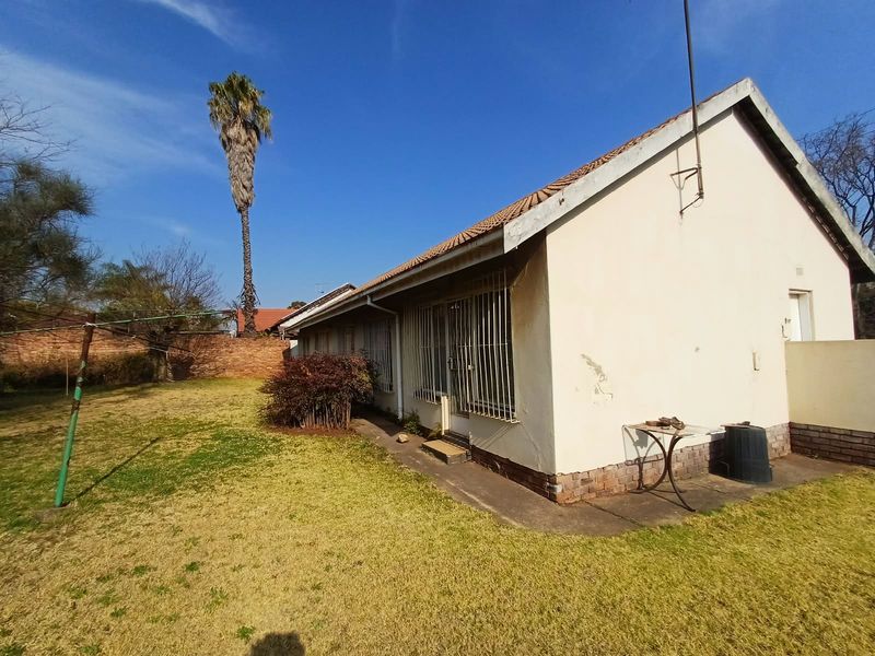 Rear view of the house featuring a tiled roof, security bars on windows, and a spacious garden with a brick boundary wall.
