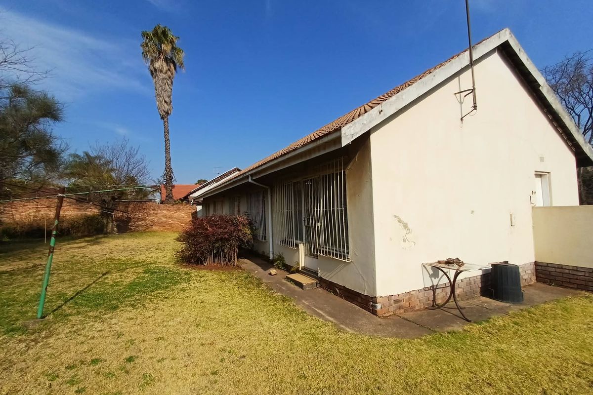 Rear view of the house featuring a tiled roof, security bars on windows, and a spacious garden with a brick boundary wall.