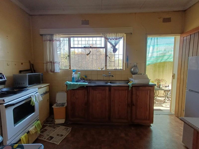 A dated kitchen featuring wooden cabinetry, a double sink, and a built-in stove, with direct access to an outdoor area.