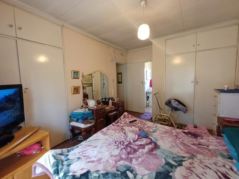 Bedroom featuring extensive built-in cupboard storage and a pendant light fixture, showing signs of wall surface wear and paint deterioration.