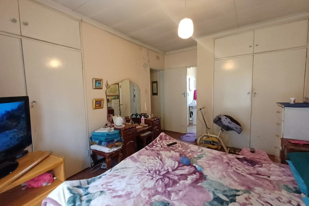 Bedroom featuring extensive built-in cupboard storage and a pendant light fixture, showing signs of wall surface wear and paint deterioration.
