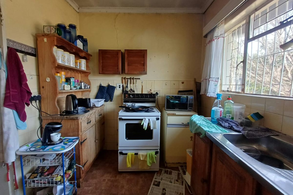A dated kitchen featuring original cabinetry, a stainless steel sink, and a tiled splashback, offering significant potential for a modern renovation.