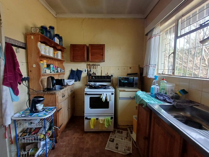A dated kitchen featuring original cabinetry, a stainless steel sink, and a tiled splashback, offering significant potential for a modern renovation.