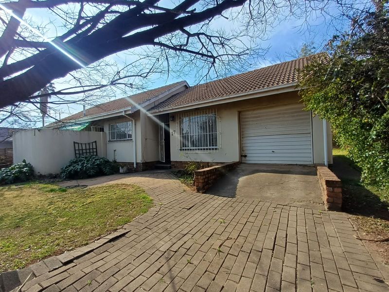 Front elevation of a single-story house featuring a tiled roof, single garage, and brick-paved driveway with established garden surroundings.