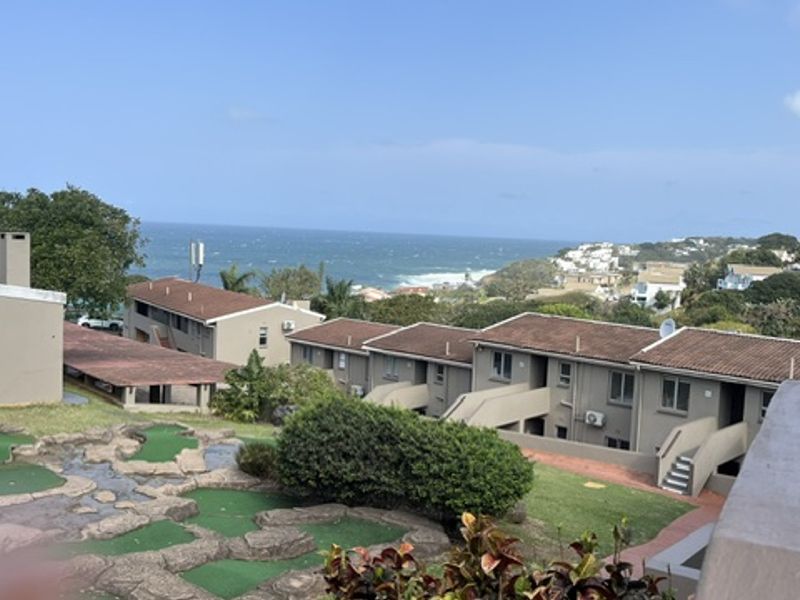 Elevated coastal view overlooking a miniature golf course, surrounding apartment complex buildings, and the ocean in the distance.
