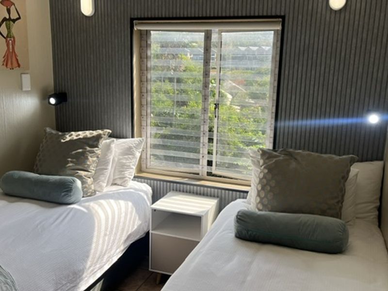 A cozy bedroom featuring twin beds, modern vertical slat wall paneling, and a window with natural light.