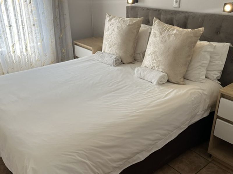 A well-maintained bedroom featuring tiled flooring, a modern upholstered headboard, and integrated wall-mounted reading lights.