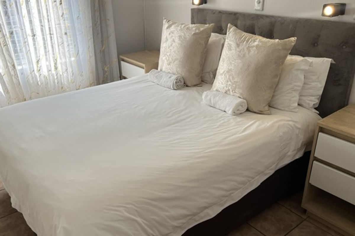 A well-maintained bedroom featuring tiled flooring, a modern upholstered headboard, and integrated wall-mounted reading lights.