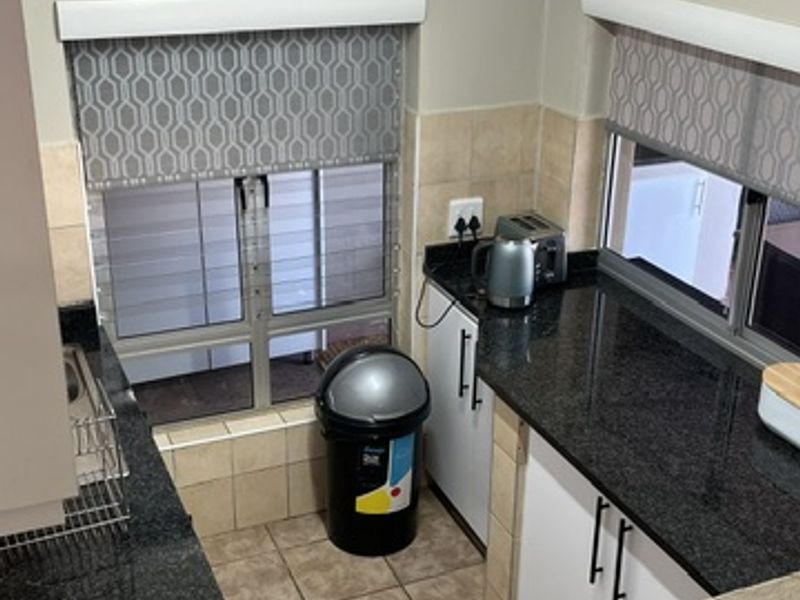 A functional kitchen featuring granite countertops, white cabinetry, tiled flooring, and a tiled backsplash, providing a practical workspace with natural light.